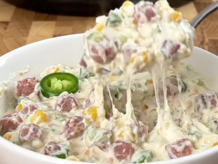 A stainless steel slow cooker filled with a creamy dip featuring sausage, corn, and jalapenos.