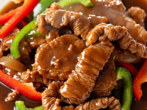 A close-up of tender pork loin strips with bell peppers and onions in a rich brown sauce.