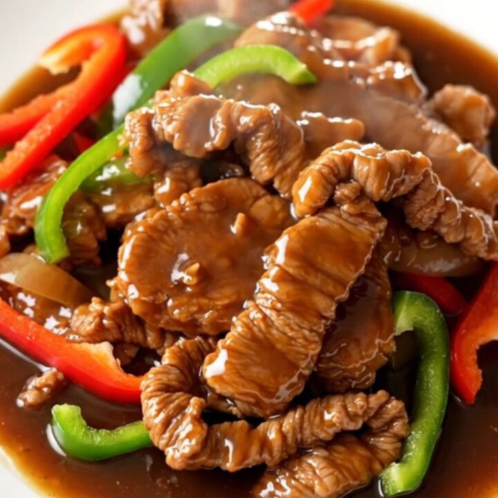 A close-up of tender pork loin strips with bell peppers and onions in a rich brown sauce.