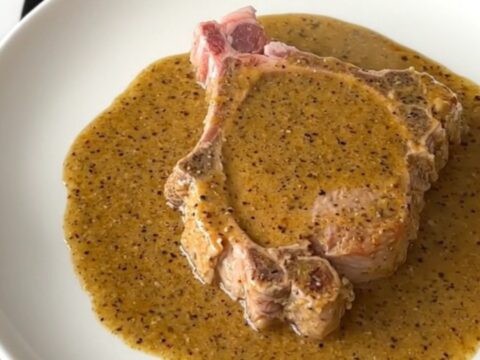 A close-up shot of a tender, slow-cooked pork chop covered in a thick, creamy peppercorn gravy.
