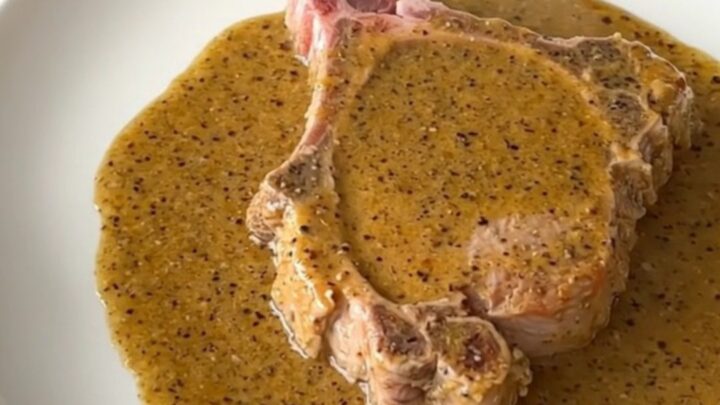 A close-up shot of a tender, slow-cooked pork chop covered in a thick, creamy peppercorn gravy.