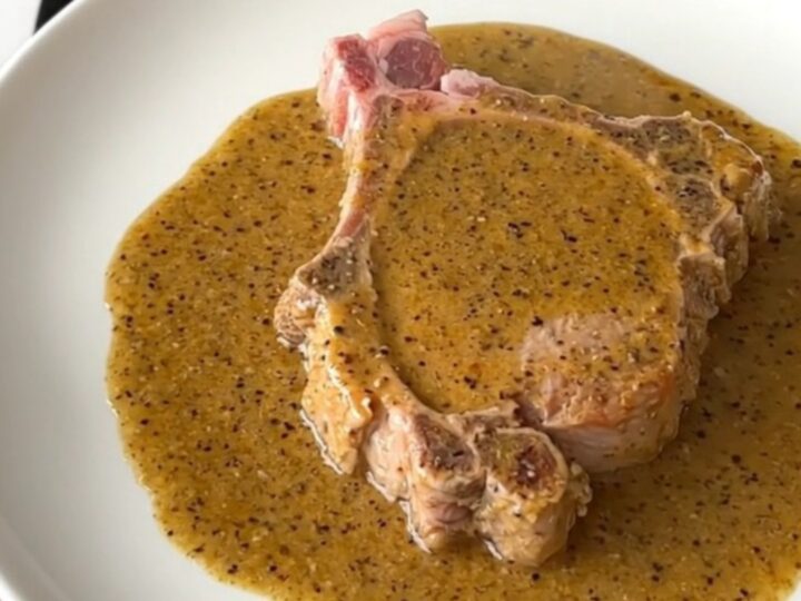 A close-up shot of a tender, slow-cooked pork chop covered in a thick, creamy peppercorn gravy.