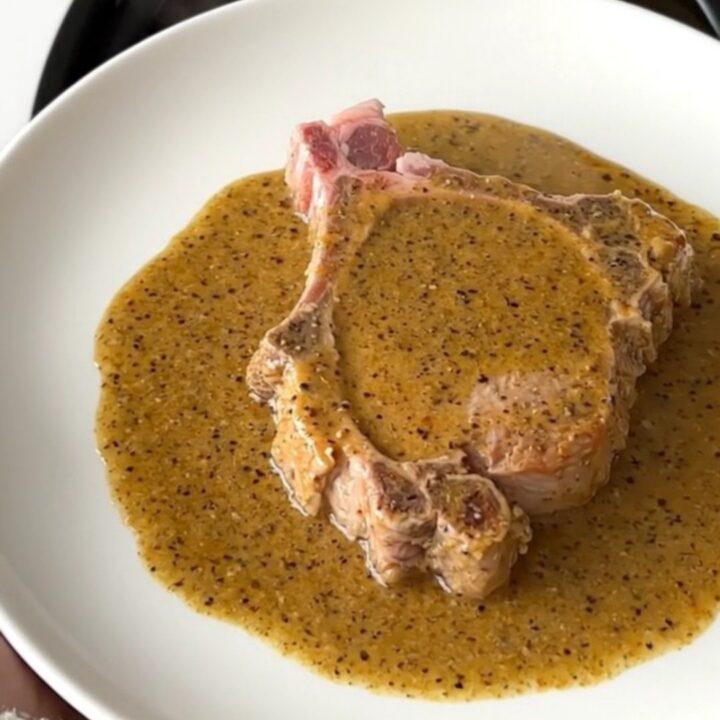 A close-up shot of a tender, slow-cooked pork chop covered in a thick, creamy peppercorn gravy.