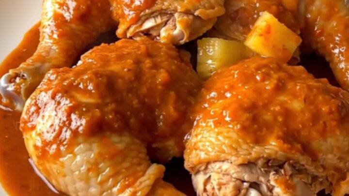 A top-down view of six raw chicken thighs in a slow cooker topped with pineapple chunks and red chile sauce.