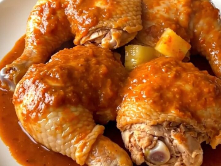 A top-down view of six raw chicken thighs in a slow cooker topped with pineapple chunks and red chile sauce.
