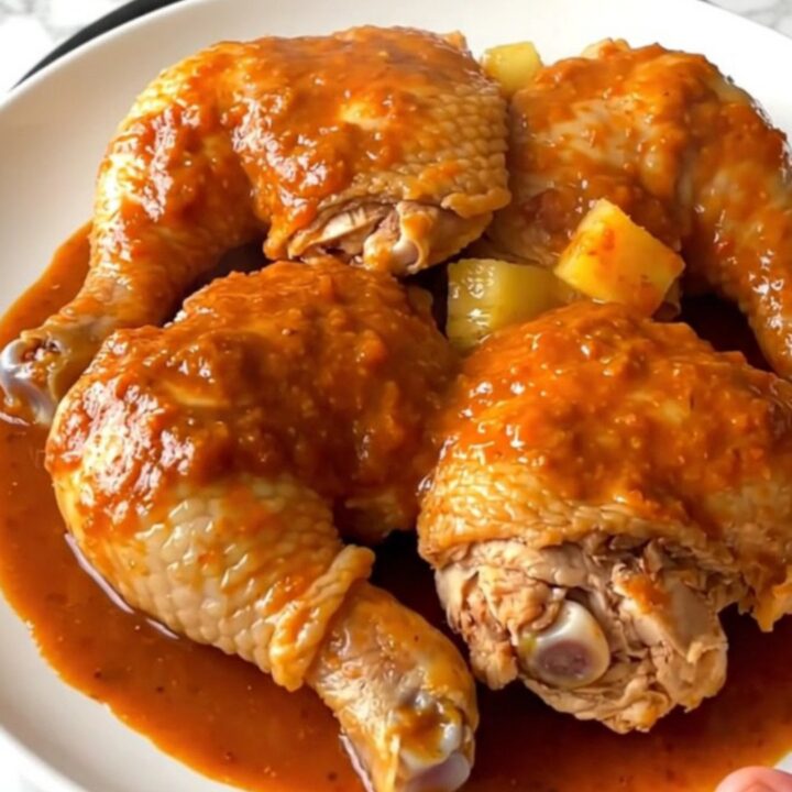 A top-down view of six raw chicken thighs in a slow cooker topped with pineapple chunks and red chile sauce.