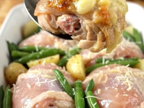 A close-up of a baked Italian chicken thigh dish with potatoes and green beans in a ceramic pan.
