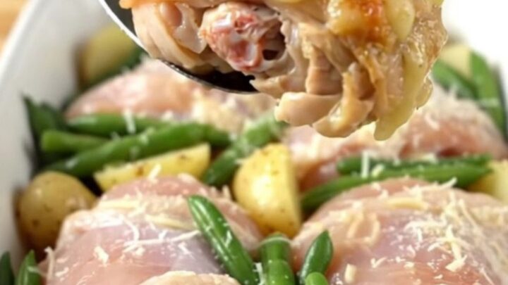 A close-up of a baked Italian chicken thigh dish with potatoes and green beans in a ceramic pan.