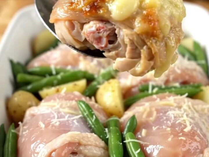 A close-up of a baked Italian chicken thigh dish with potatoes and green beans in a ceramic pan.