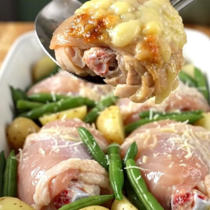 A close-up of a baked Italian chicken thigh dish with potatoes and green beans in a ceramic pan.