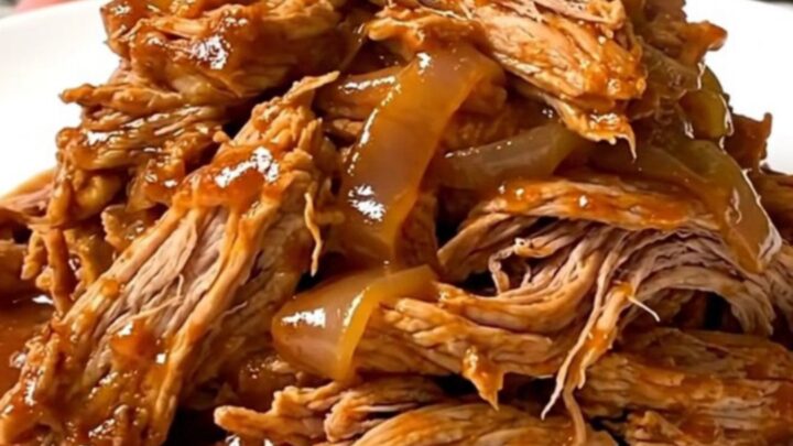 A close-up view of tender, shredded pork tinga in a rich, smoky red sauce on a white plate.