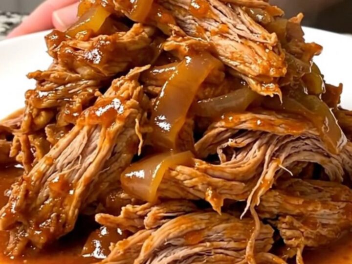A close-up view of tender, shredded pork tinga in a rich, smoky red sauce on a white plate.