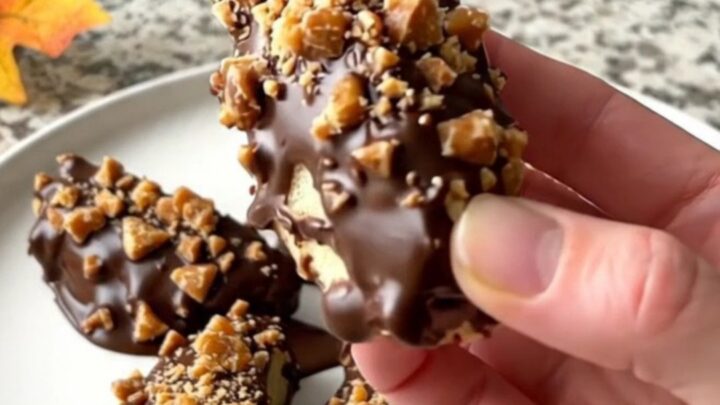 A close-up of chocolate-dipped green apple wedges topped with toffee bits on a parchment-lined tray.