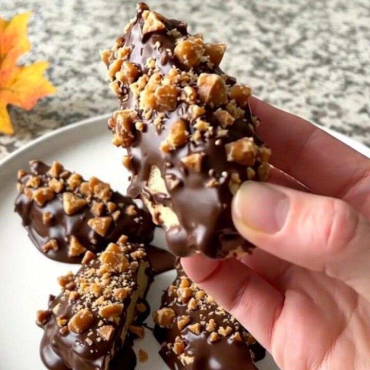 A close-up of chocolate-dipped green apple wedges topped with toffee bits on a parchment-lined tray.