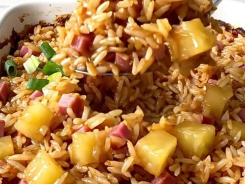 A top-down view of a rectangular baking dish filled with rice, ham, and pineapple pieces.