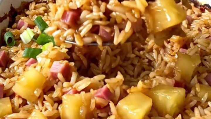 A top-down view of a rectangular baking dish filled with rice, ham, and pineapple pieces.