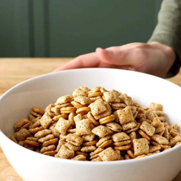 A stainless steel slow cooker filled with a golden, toasted mixture of cereal, pretzels, and peanuts.