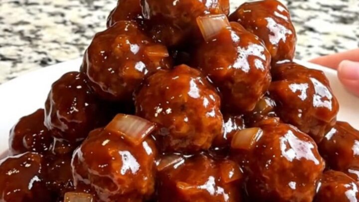 A top-down view of frozen beef meatballs in a black slow cooker, ready to be seasoned with onion, ginger, and plum sauce.