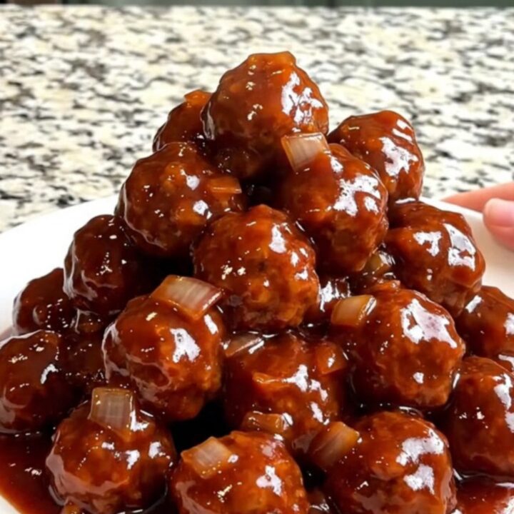 A top-down view of frozen beef meatballs in a black slow cooker, ready to be seasoned with onion, ginger, and plum sauce.