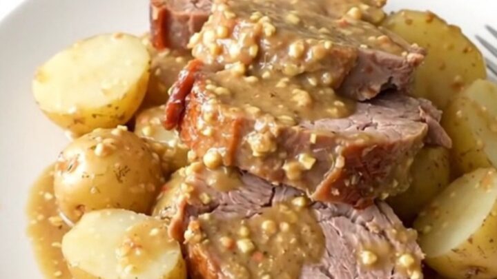 A rustic platter featuring a perfectly sliced, tender pork loin surrounded by soft baby potatoes in a rich Dijon sauce.