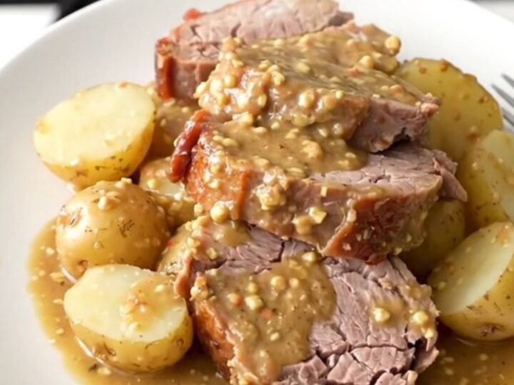 A rustic platter featuring a perfectly sliced, tender pork loin surrounded by soft baby potatoes in a rich Dijon sauce.