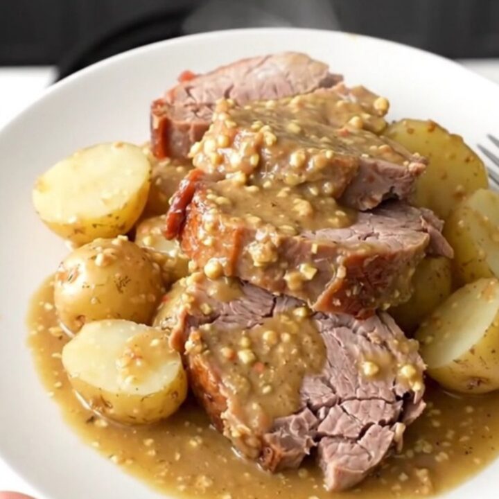 A rustic platter featuring a perfectly sliced, tender pork loin surrounded by soft baby potatoes in a rich Dijon sauce.