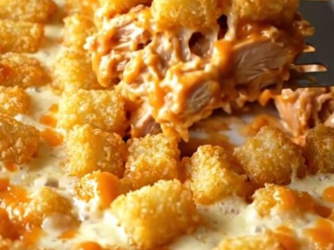 A top-down view of a golden, cheesy buffalo chicken potato tot casserole in a white ceramic dish.
