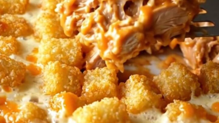 A top-down view of a golden, cheesy buffalo chicken potato tot casserole in a white ceramic dish.