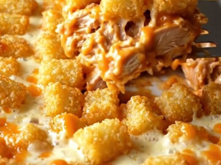 A top-down view of a golden, cheesy buffalo chicken potato tot casserole in a white ceramic dish.