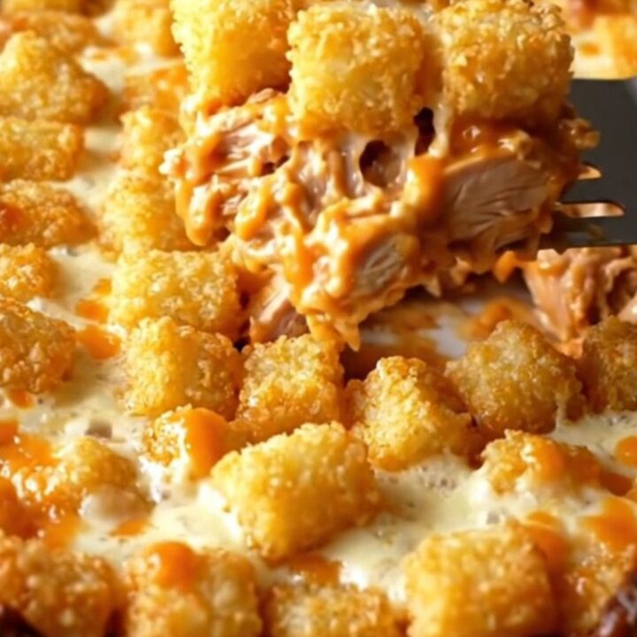 A top-down view of a golden, cheesy buffalo chicken potato tot casserole in a white ceramic dish.