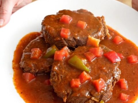 A close-up of tender pieces of round steak in a rich tomato-based Creole gravy with visible bell peppers and onions.