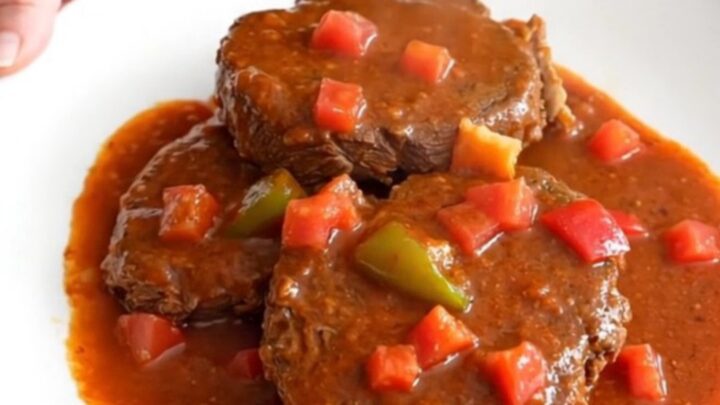 A close-up of tender pieces of round steak in a rich tomato-based Creole gravy with visible bell peppers and onions.