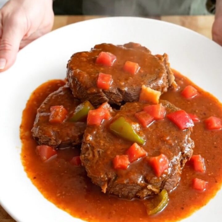 A close-up of tender pieces of round steak in a rich tomato-based Creole gravy with visible bell peppers and onions.