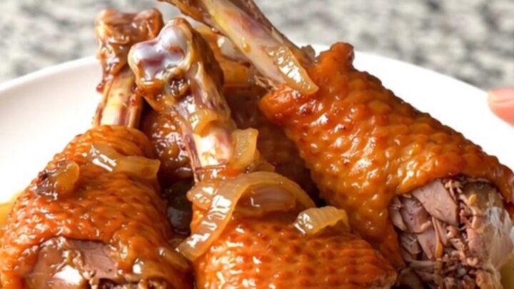 Four slow-cooked turkey legs with onions in a black slow cooker bowl.