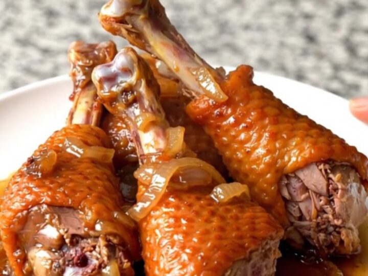 Four slow-cooked turkey legs with onions in a black slow cooker bowl.