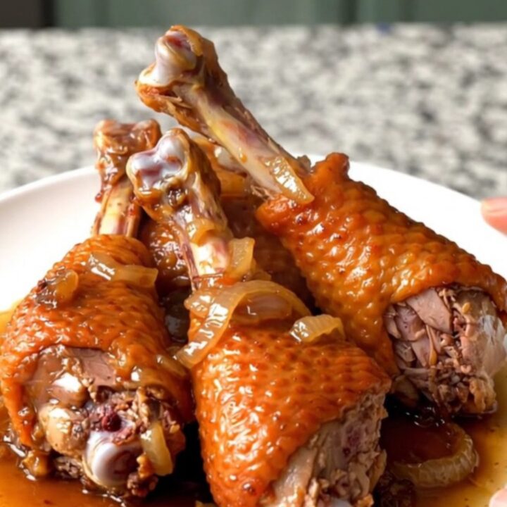 Four slow-cooked turkey legs with onions in a black slow cooker bowl.
