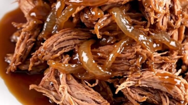 A close-up of tender, shredded maple bourbon pork served on a white plate with a glossy, dark sauce.