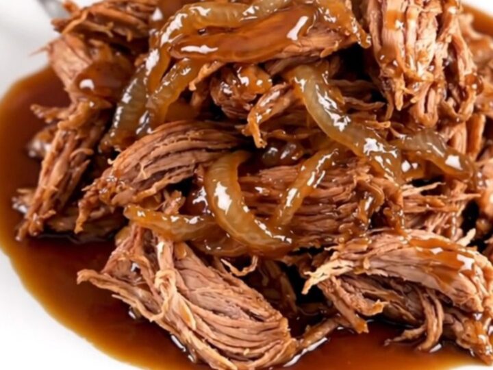 A close-up of tender, shredded maple bourbon pork served on a white plate with a glossy, dark sauce.