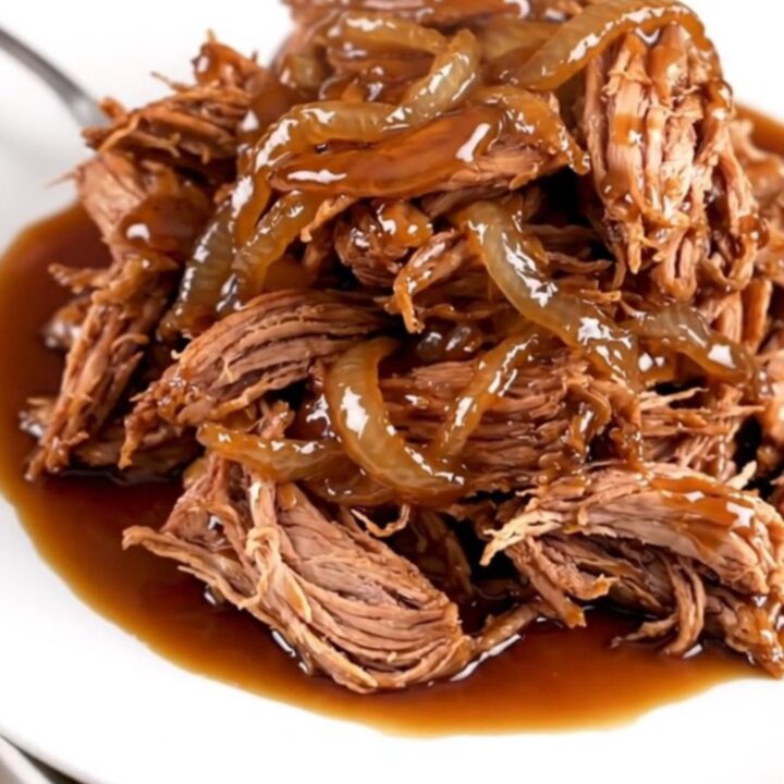 A close-up of tender, shredded maple bourbon pork served on a white plate with a glossy, dark sauce.