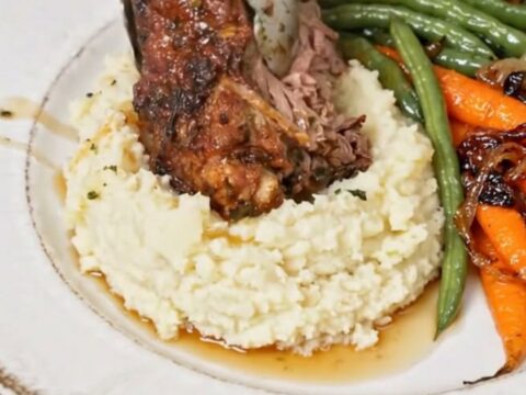 A succulent braised beef shank served on a bed of creamy mashed potatoes with glazed carrots and green beans.