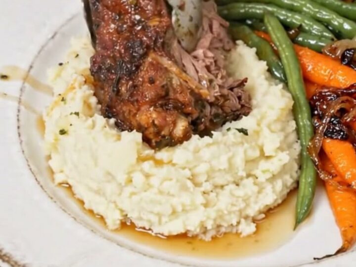 A succulent braised beef shank served on a bed of creamy mashed potatoes with glazed carrots and green beans.