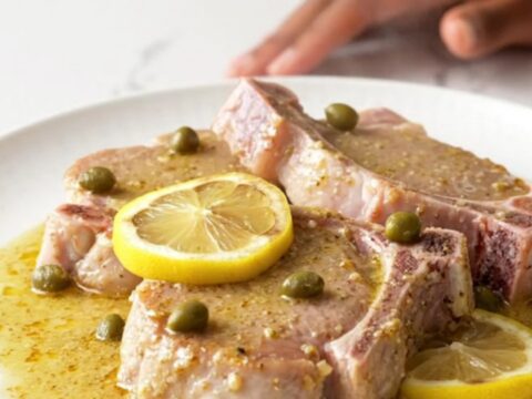 Close-up of creamy pork piccata with lemon slices and capers in a slow cooker.