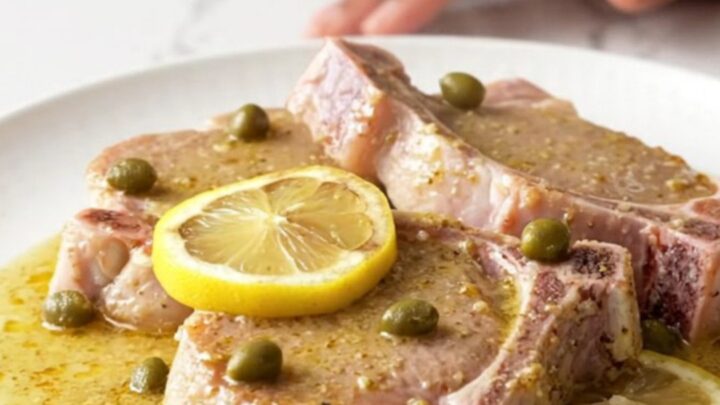Close-up of creamy pork piccata with lemon slices and capers in a slow cooker.