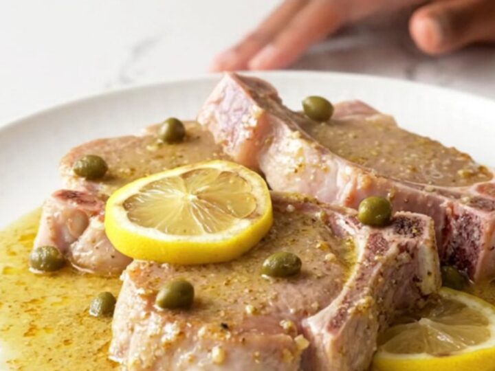 Close-up of creamy pork piccata with lemon slices and capers in a slow cooker.