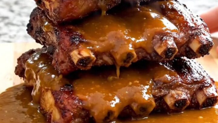 A close-up of tender, saucy honey sriracha country-style ribs being lifted from a black slow cooker with a serving spoon.