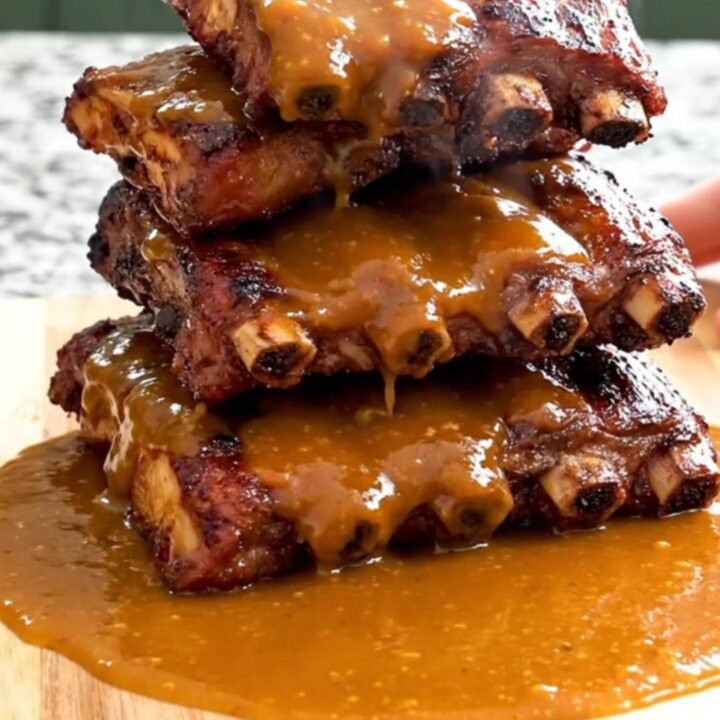 A close-up of tender, saucy honey sriracha country-style ribs being lifted from a black slow cooker with a serving spoon.