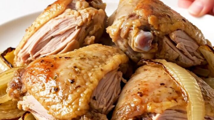 A top-down view of raw turkey thighs and red onion wedges inside a slow cooker, seasoned with colorful spices.