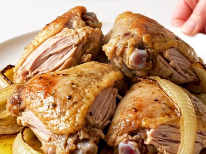 A top-down view of raw turkey thighs and red onion wedges inside a slow cooker, seasoned with colorful spices.