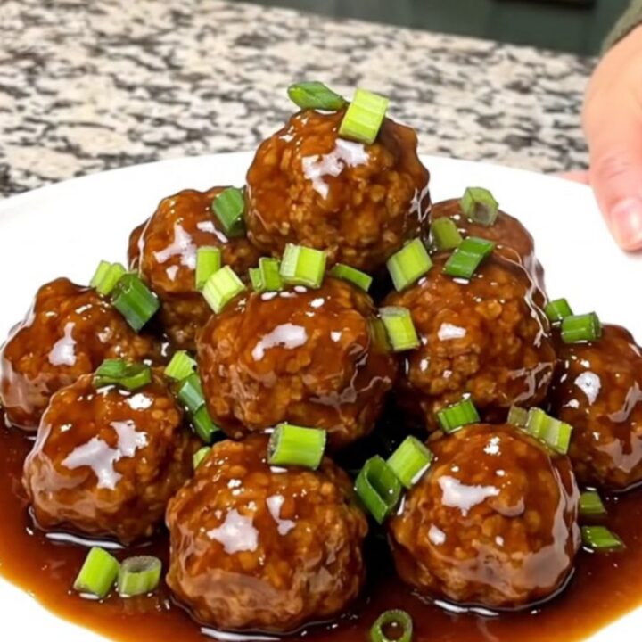 A close-up of tender turkey meatballs coated in a glossy hoisin sauce served on a white plate.