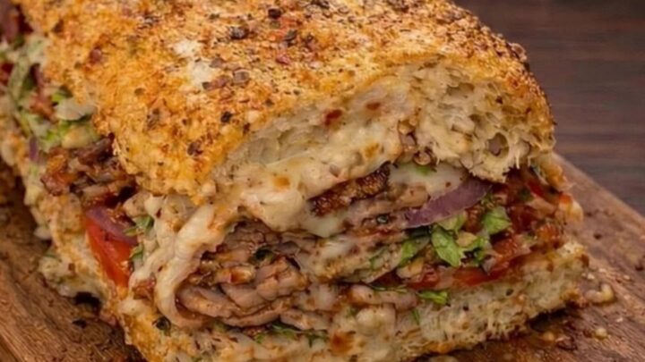 A crispy, toasted Italian melt sandwich sliced in half, showing thick, melted mozzarella stretching between the layers.